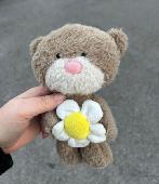 Little small teddy bear that's holding up a Daisy flower. 