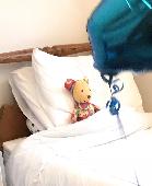 A brightly multi- coloured fabric teddy with one ear larger than the other. It i