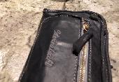 A black bigger wallet in leather with leather fringed on one side and a zip on t